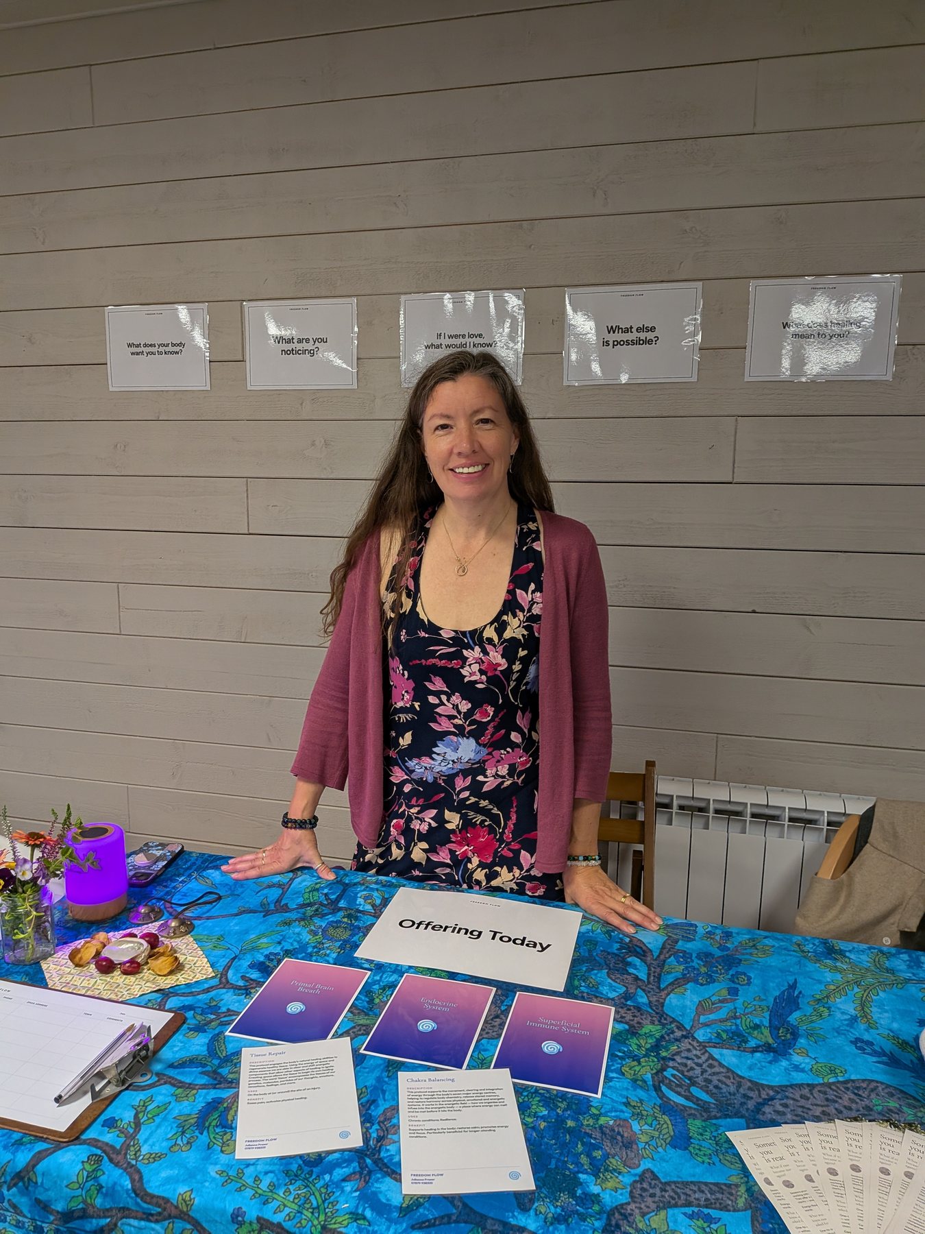 Julianne Fraser at her offerings table at Heligan, smiling, with cards asking what else is possible