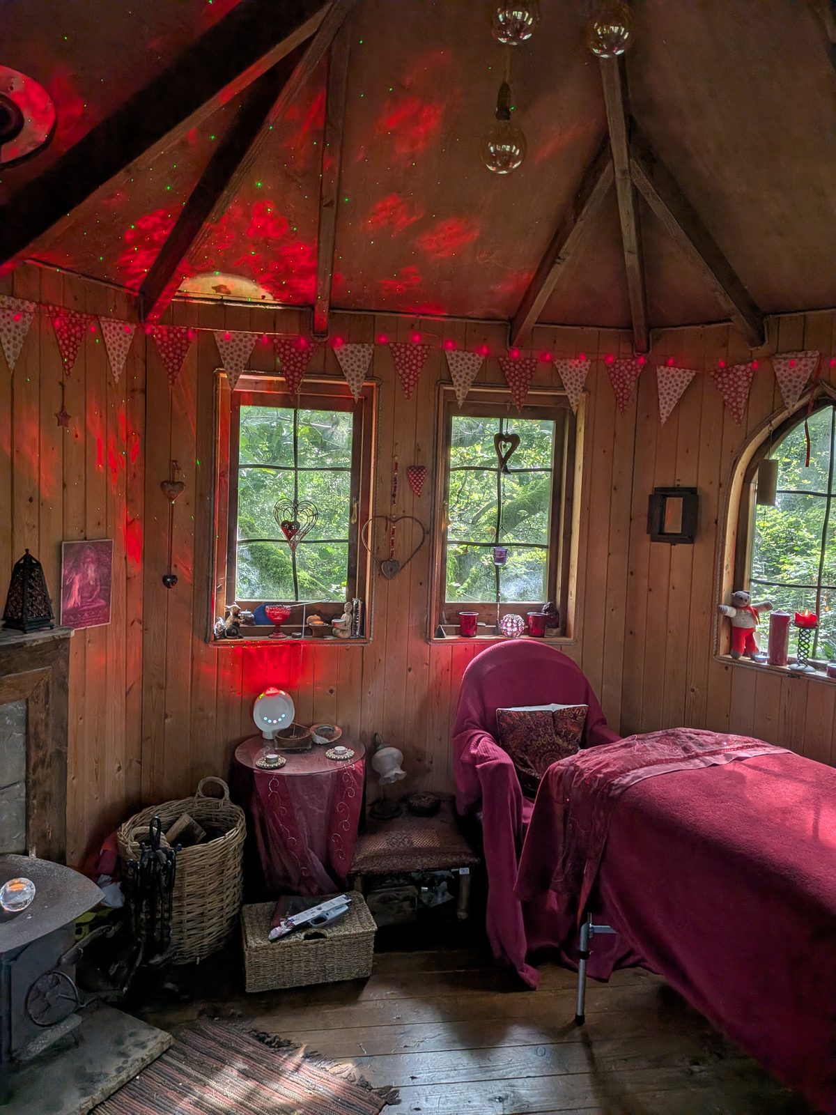 The treatment room at Rainbow's End: a timber tree-house with a couch, a wood stove, and windows onto the woodland